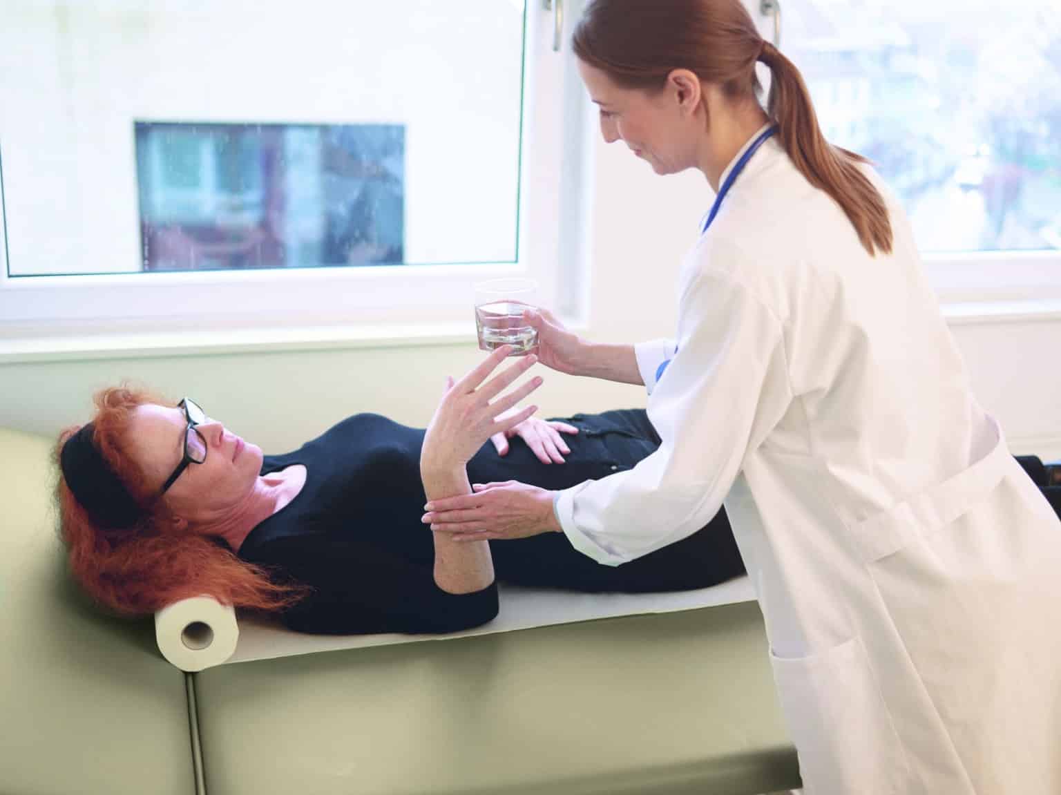 Doctor offering a glass of water to a patient lying on a medical examination bed