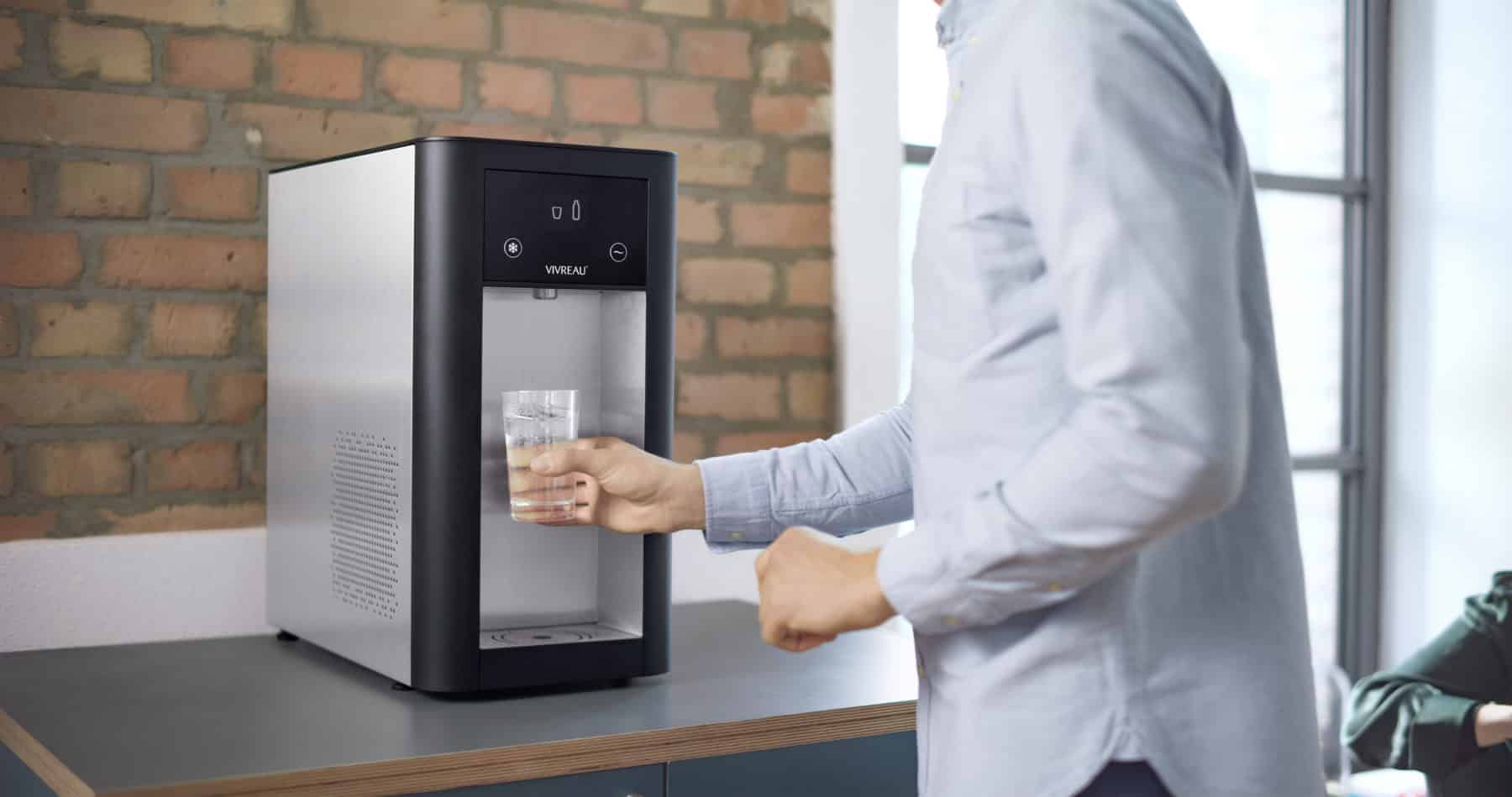 Person filling a glass of water from a Vivreau countertop dispenser