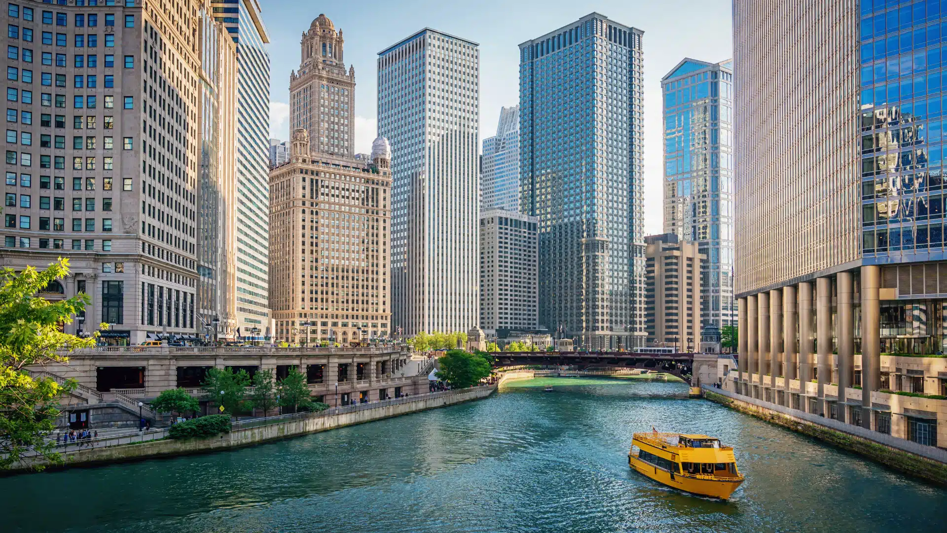 Yellow boat cruising along a river surrounded by tall modern skyscrapers and historic buildings in a bustling urban setting