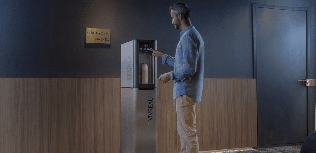 Man using a Vivreau water dispenser in a hotel hallway