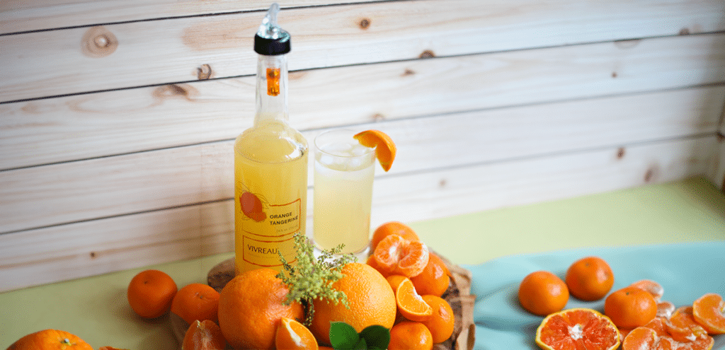 Vivreau Orange Tangerine flavor bottle surrounded by fresh oranges and tangerines