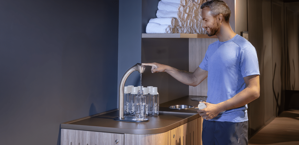 Man filling Vivreau water bottle at a modern water dispenser in a wellness center