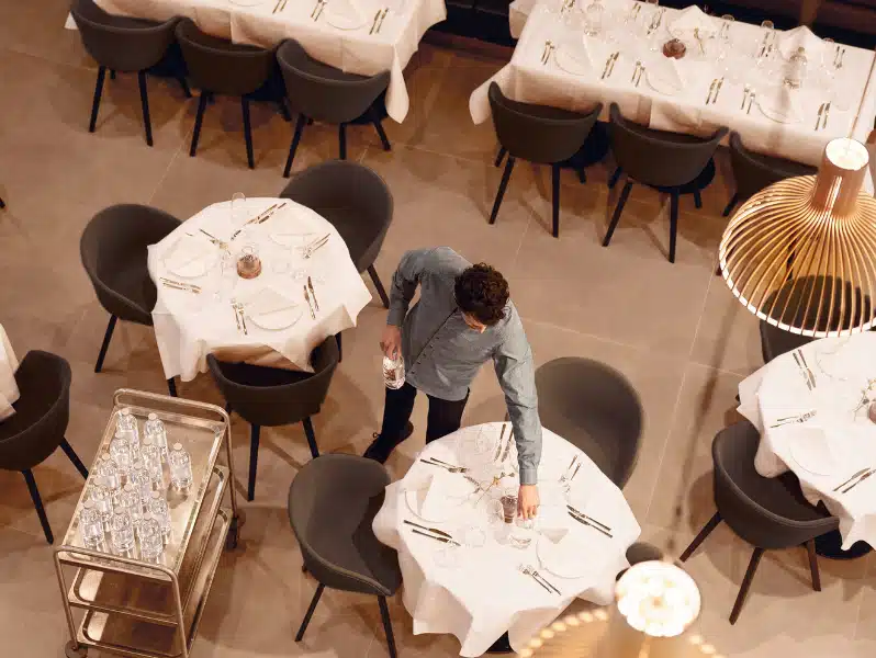 Waiter preparing dining tables with glass water bottles in a restaurant